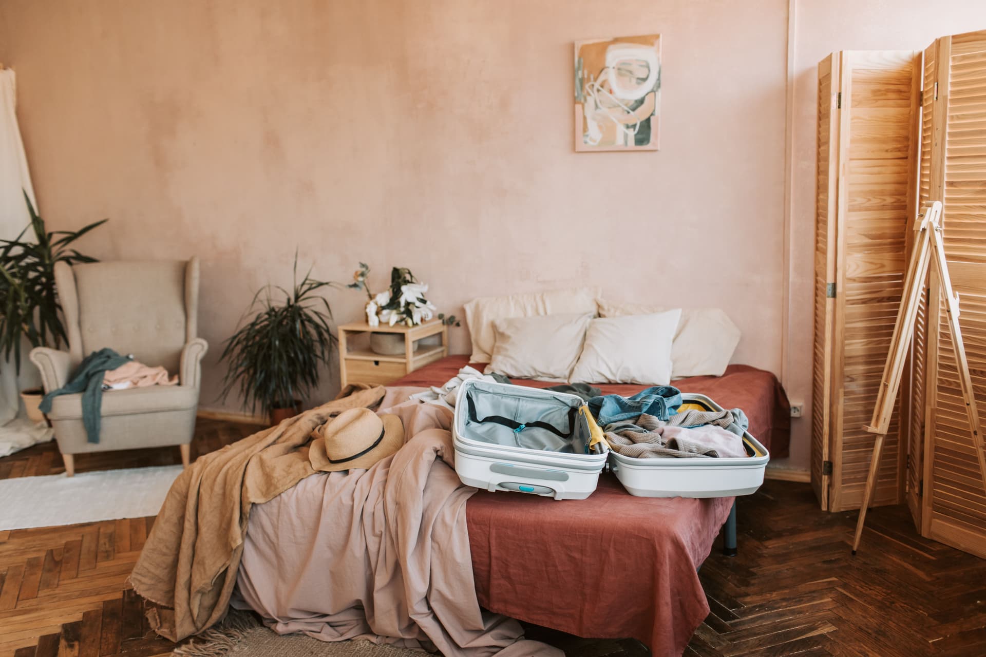 An open suitcase lying on a bed in a warmly lit bedroom, part packed.
